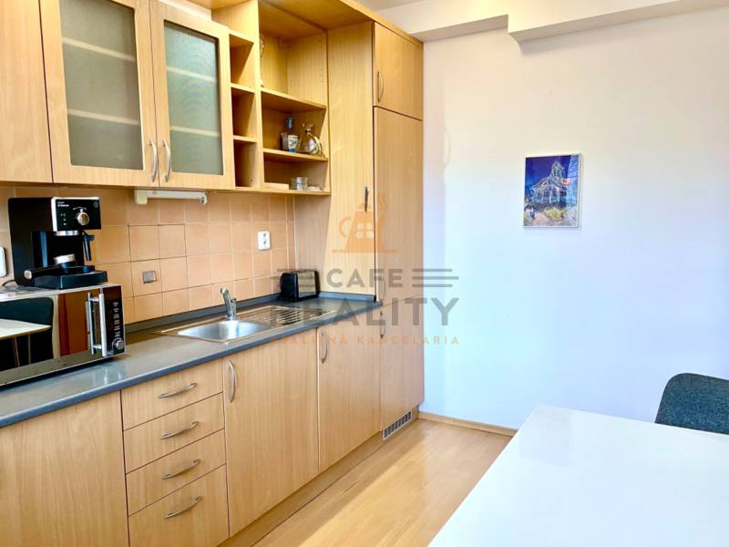 A kitchen in a 2-room apartment with a wooden decor floor and a wooden kitchen unit.