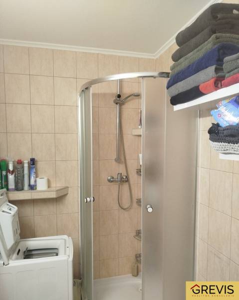 A bathroom in a studio apartment with a washing machine, shower, shelf, and stored towels.