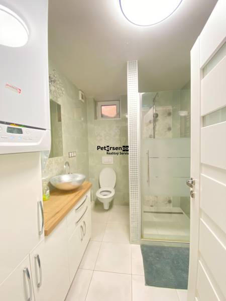 A bathroom in a family house with a sink, shower, and toilet, with light tiles.
