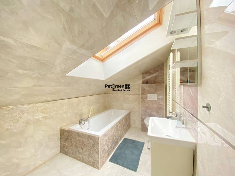 A bathroom in a family house with a bathtub, a skylight, and light tiles.
