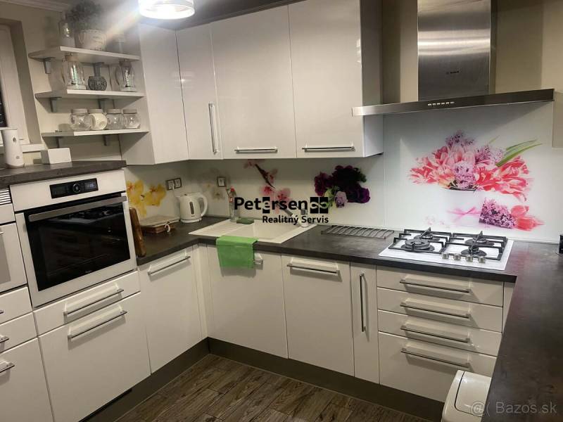 A kitchen in a family house with white cabinets, decorative tiles, and a wooden-patterned floor.