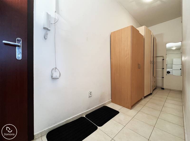 Hallway in a one-room apartment with white walls, tiles, and cabinets.