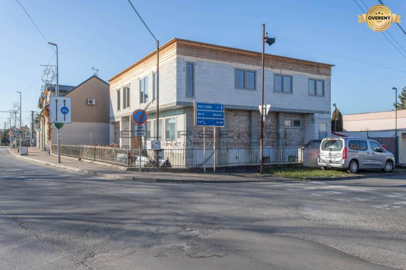 A building in Veľké Leváre, by the road, with a parked car and traffic signs.