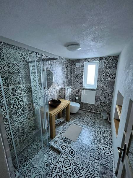 A bathroom in a family house with ornamental tiles, a shower corner, and a sink on a wooden table.