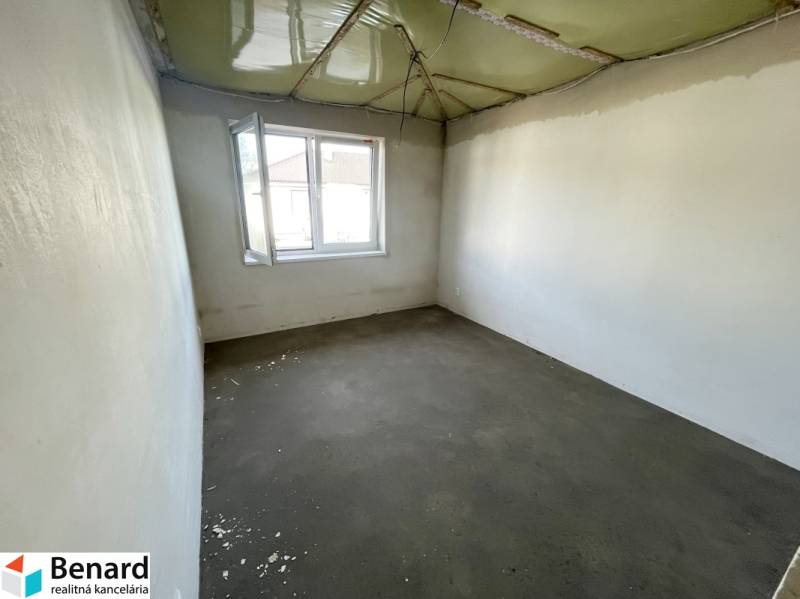 An empty room in a family house without flooring and with a green ceiling.