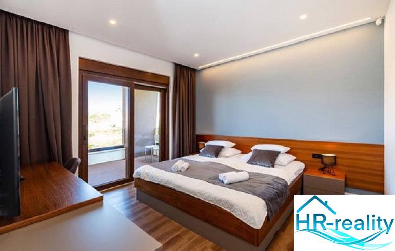 Room with a bed in the villa, floor with wooden decor, balcony with a view.