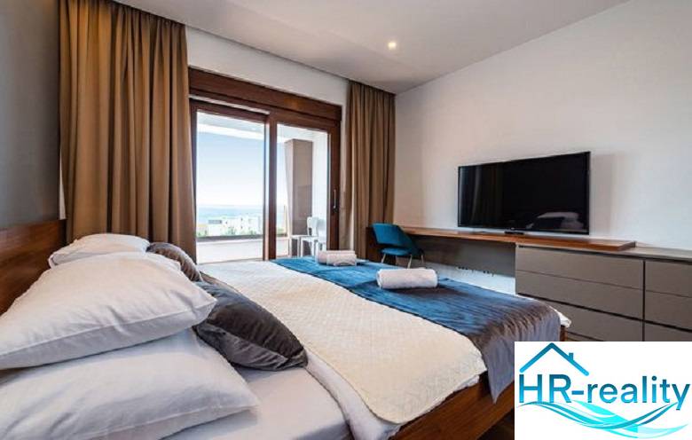 Bedroom in a villa with wood-patterned flooring, a bed, a TV, and a view of the terrace.