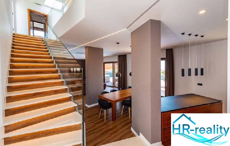 Interior of a villa with wooden flooring, staircase, and dining table.