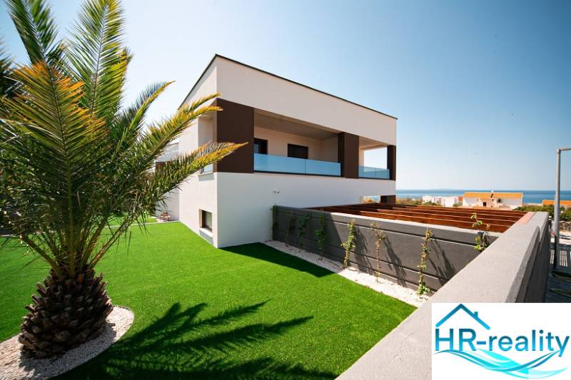 A villa in Novalja with a sea view, surrounded by a lawn and a palm tree.