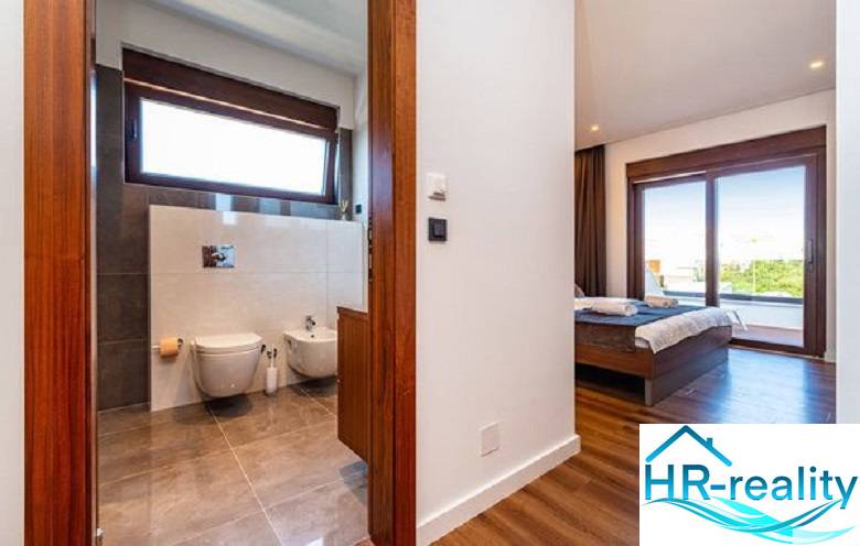 Interior of a villa with wood-decor flooring, bedroom and bathroom with a large window.