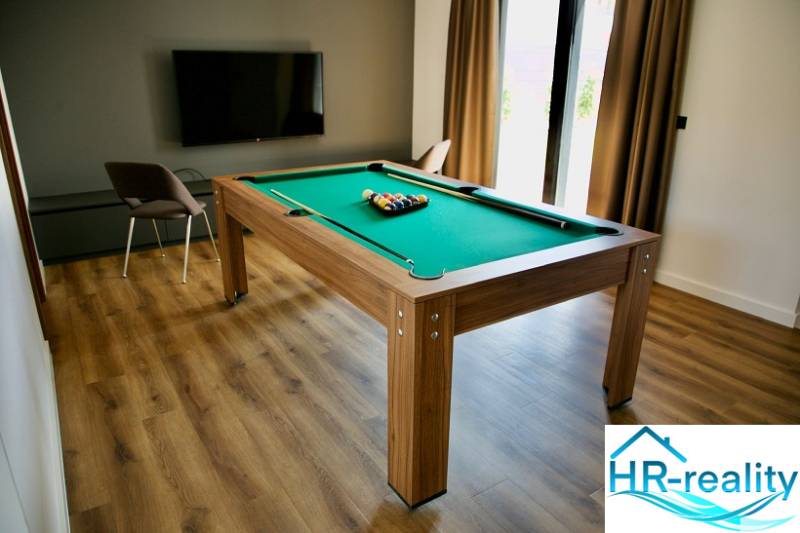 A room in a villa with a billiard table, television, and a wooden decor floor.