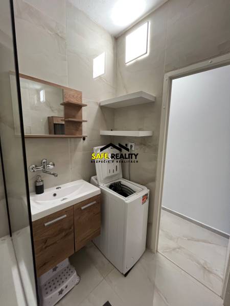 Bathroom in a 3-room apartment with a sink, washing machine, and shelves, stone-patterned floor.