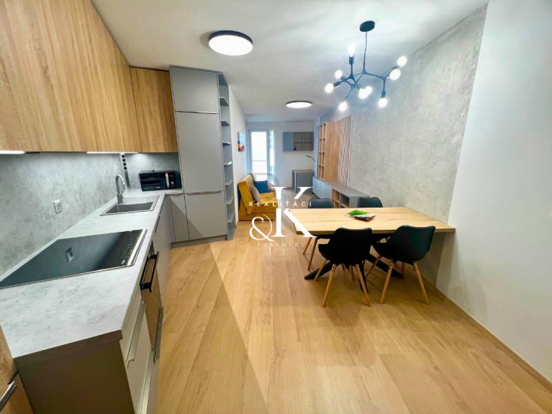 A kitchen in a 2-room apartment with a wooden decor floor, a dining table, and a modern light fixture.
