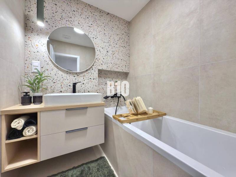 A bathroom with a sink, bathtub, round mirror, and decorative wall in a 3-room apartment.