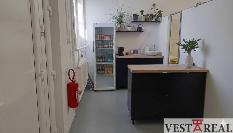 A small kitchenette in the warehouse and hall area with a refrigerator and plants.
