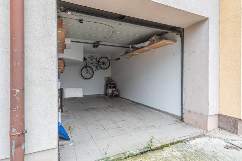 Garage space with tiles, a bicycle on the wall, and a wooden shelf.
