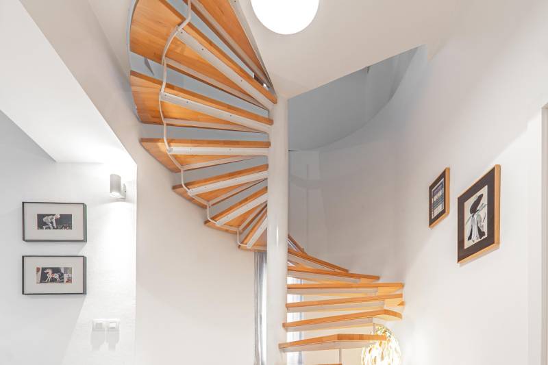 A spiral staircase with a wooden decor floor in a 4-room apartment. There are paintings on the walls.