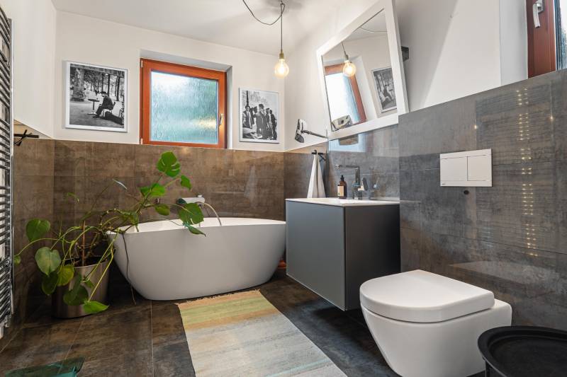 Bathroom in a 4-room apartment with a bathtub, large mirror, and plant, floor with wood decor.