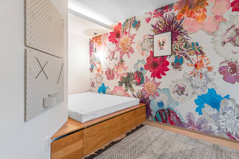 A bedroom in a 4-room apartment with colorful floral wallpaper, a bed, and a wooden storage cabinet.