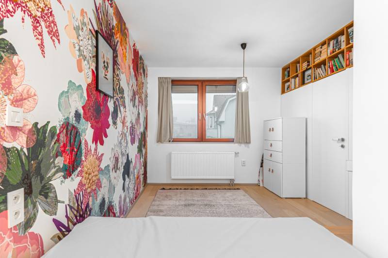 A room with patterned floral wallpaper, a bookshelf, a chest of drawers, and a wooden decor floor in a 4-room apartment.