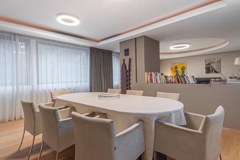 Dining room in a 4-room apartment, large oval table, wooden decor flooring, bookshelf.