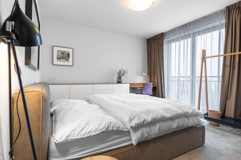 A bedroom in a 4-room apartment with a large window, a desk, and a comfortable bed.