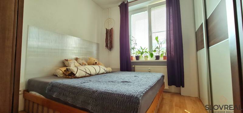 A bedroom in a 2-room apartment with light streaming through the window and a floor with a wood decor.