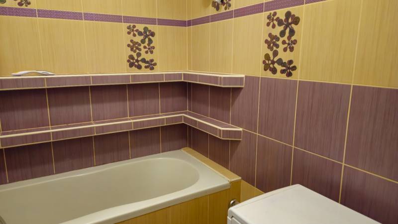 Bathroom in a 2-room apartment with tiles and a bathtub, decorated with floral patterns.