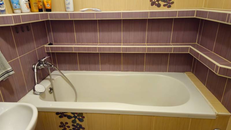 Bathroom with a bathtub, purple tiles, and a showerhead in a 2-room apartment.