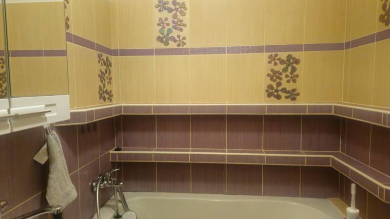 A bathroom with colorful tiles and a bathtub, decorative flowers, and a shelf in a two-room apartment.