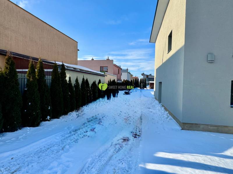 Snow-covered Gyňovská Street in Čaňa with family houses and a hedge.