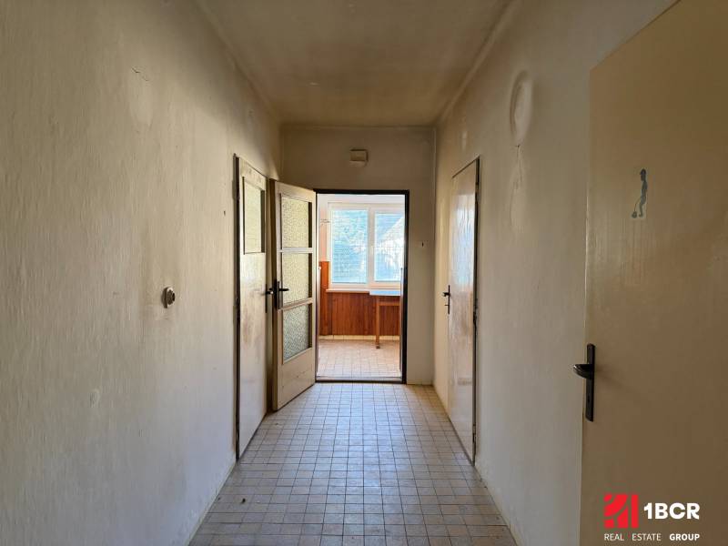 A hallway in a family house with tiles leads to a well-lit room.