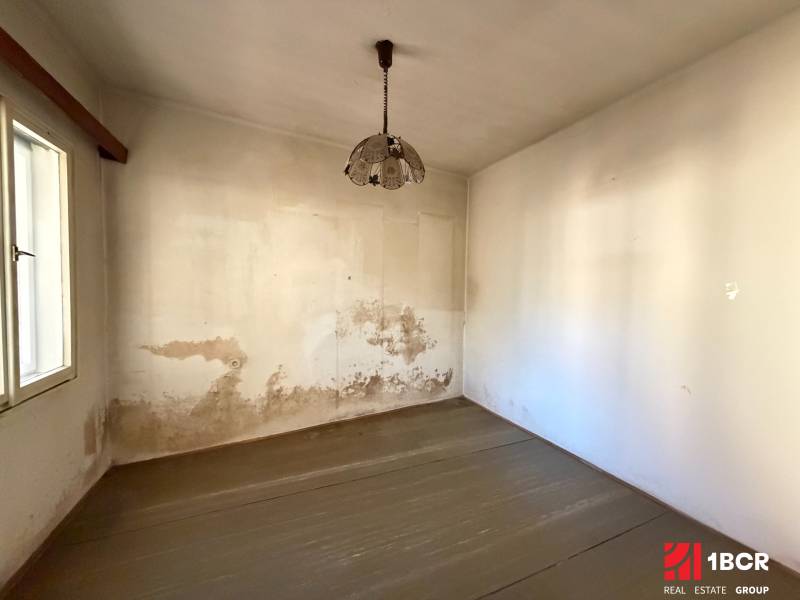 A room in a family house with a wooden decor floor and peeling walls.