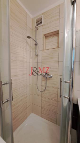 A shower corner in a 2-room apartment with cream-colored tiles and glass doors.