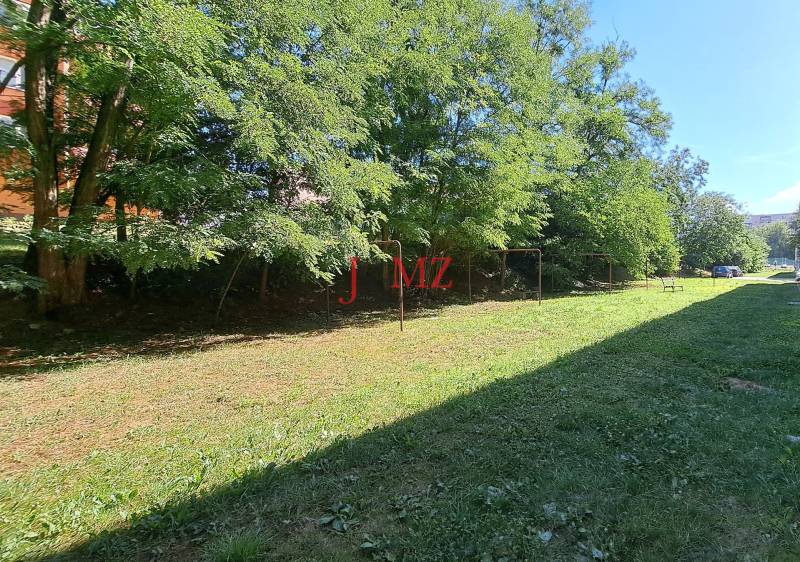 A flat grassy area with swings and trees in the town of Tlmače.