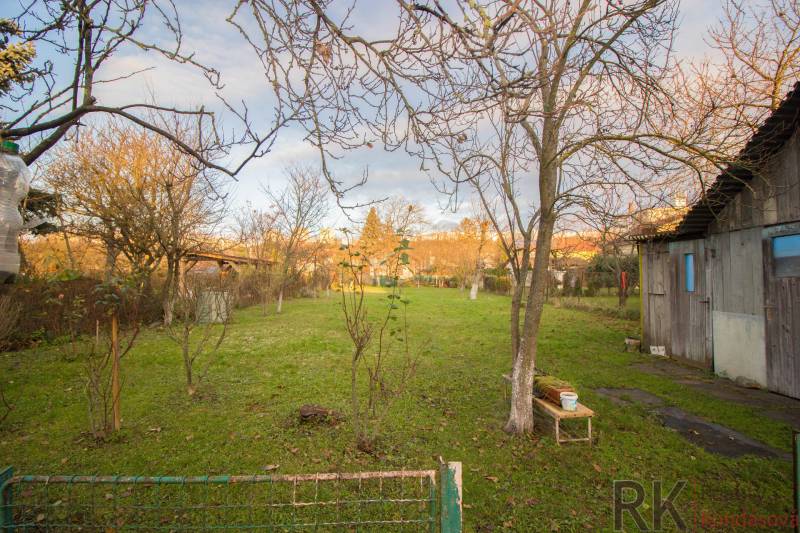 A garden with a lawn, trees, and a wooden building by a family house on Člnková Street, Košice.