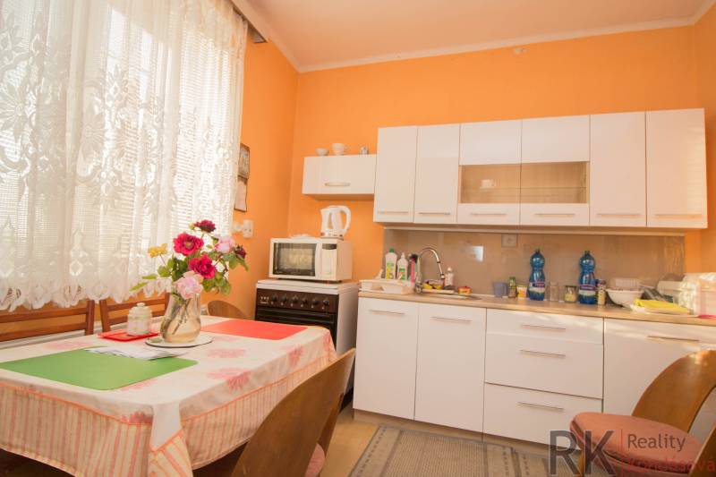 A kitchen in a family house with white furniture, a dining table, and flowers in a vase.
