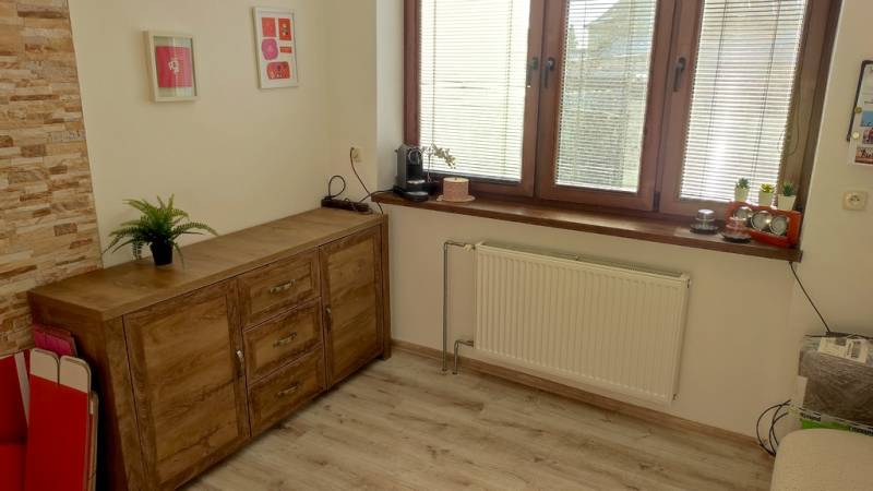 Office with a chest of drawers, flowers, and a wooden-patterned floor.