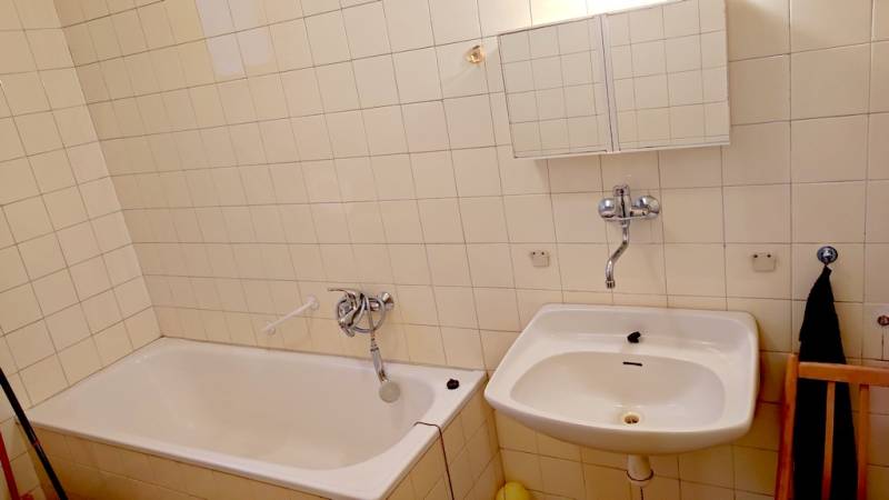 Bathroom with a bathtub, sink, and white tiles on the walls.