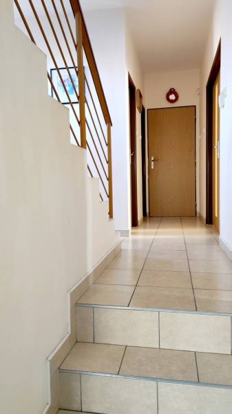 A hallway in the offices with tiles, stairs, and wooden railing leads to the door.