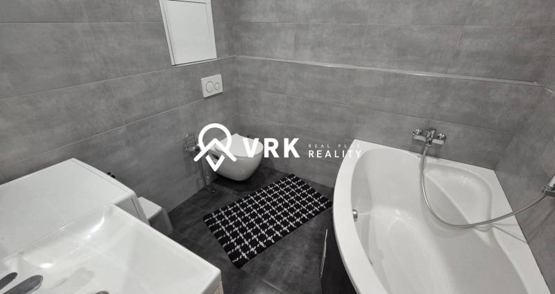 A bathroom in a 2-room apartment with a bathtub, toilet, and washing machine, tiled with gray tiles.