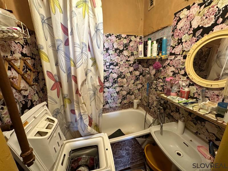 A bathroom with floral wallpaper, a washing machine, and a sink in a 3-room apartment.