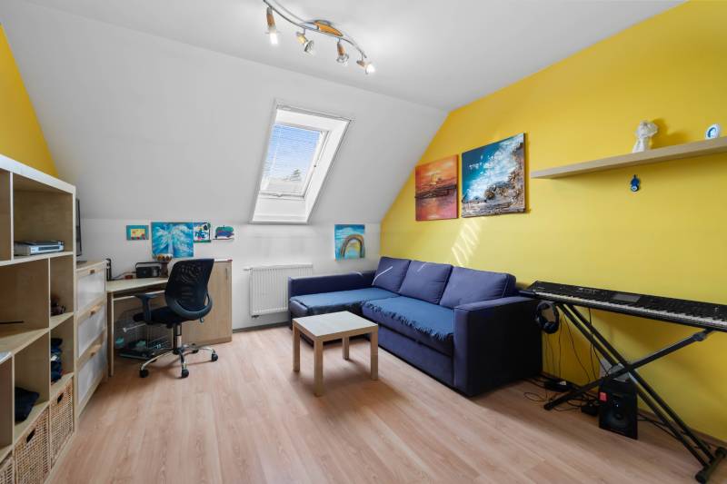 Attic room in a family house with a comfortable sofa, keyboard, and desk.
