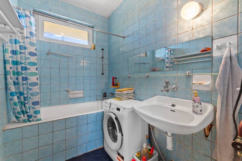 Bathroom with a sink, bathtub, and washing machine in a family house. Blue tiles and a shower curtain.