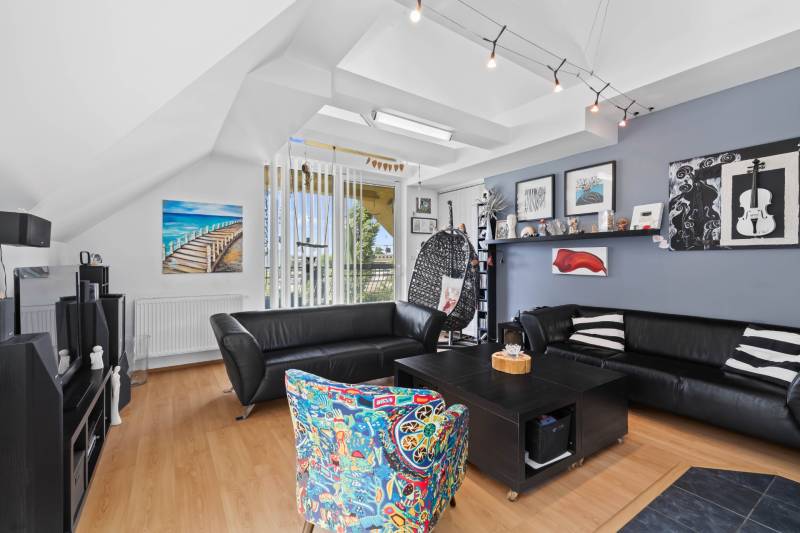 Living room in a family house with black sofas, a colorful armchair, and decorations on the walls.