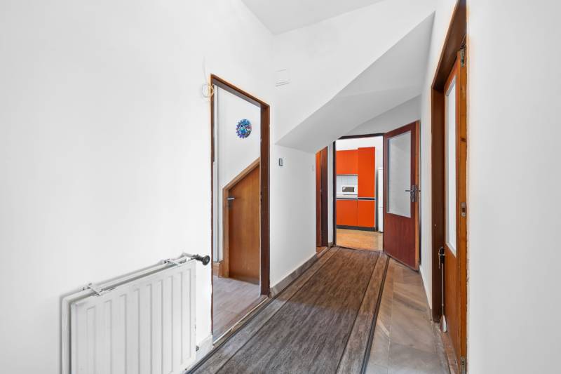 A hallway in a family house with doors leading to a kitchen with orange kitchen cabinets.