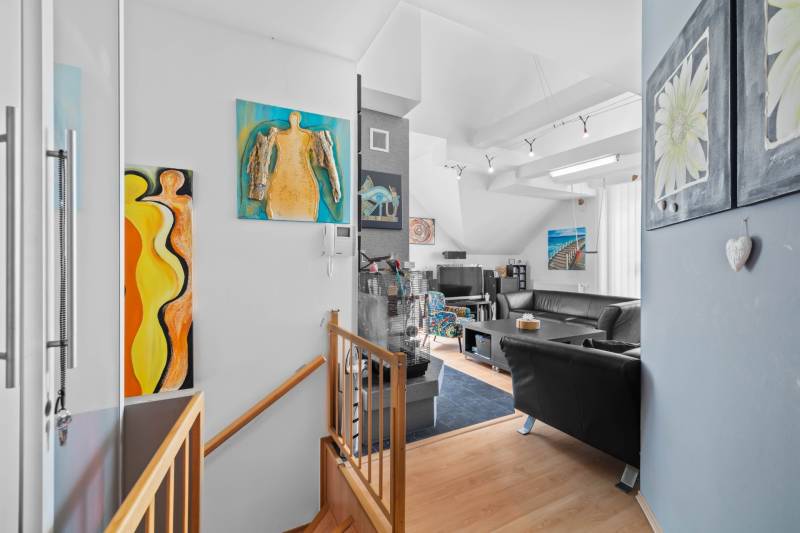 Living room with art paintings, black leather sofas, and a wooden staircase in a family house.