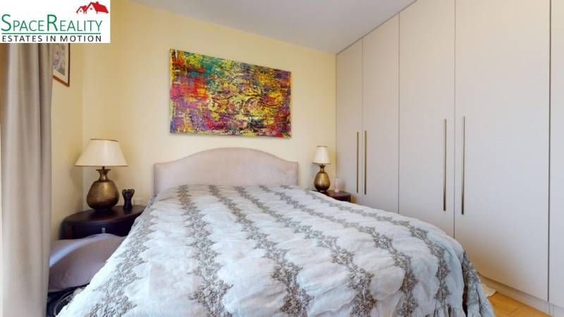 Bedroom in a family house with a large bed, colorful painting, and wardrobes.