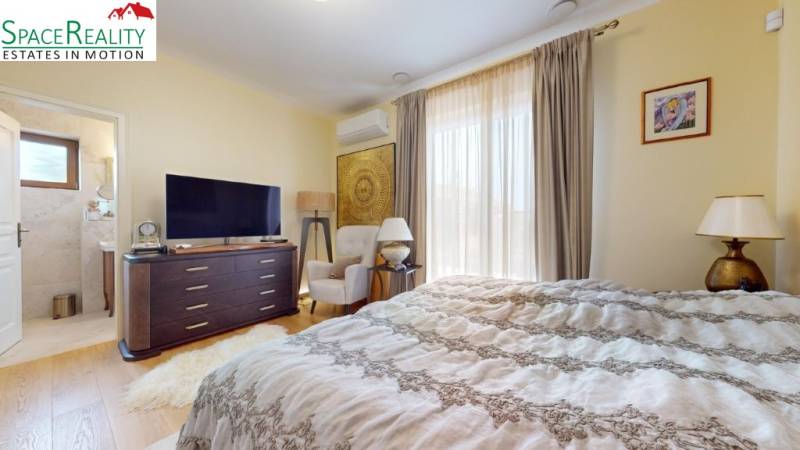 Bedroom with a TV, chair, and bed in a family house, with a wooden decor floor.