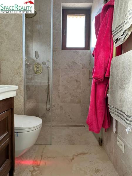A bathroom in a family house with stone tiles, a shower, and a window.